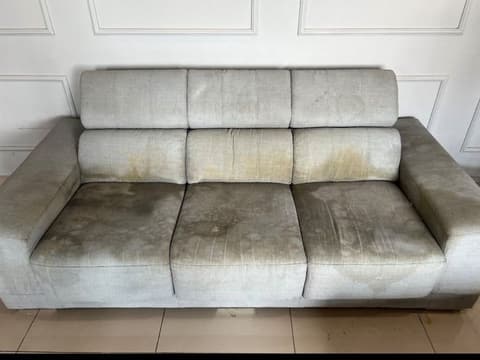 A grey three-seat fabric sofa with dark build-up on the seats and backrest, before cleaning